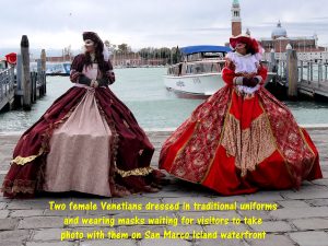 Venetian ladies in traditional costumes and wearing masks on waterfront